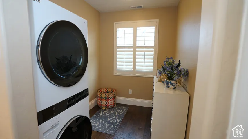 Laundry area featuring stacked washer and dryer unit, plantation shutters, and wood-finish flooring