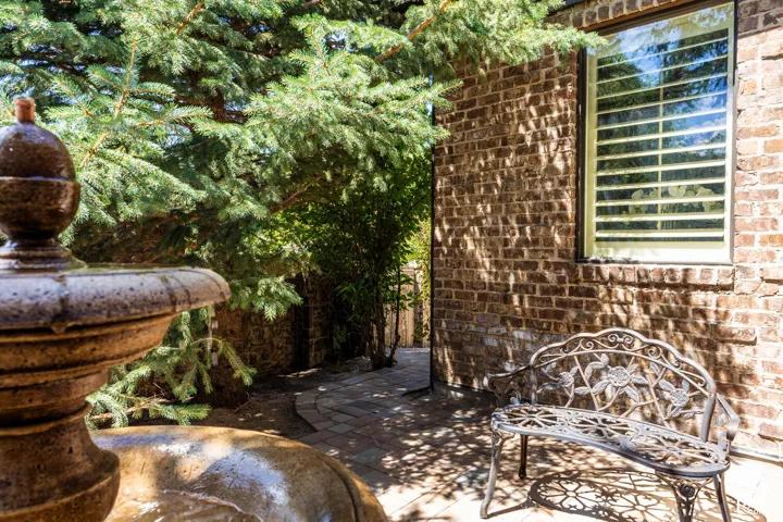 Brick exterior, paver walkway, mature evergreen landscaping, and a window with horizontal blinds