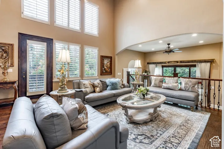 Double-height ceilings, multiple windows with white plantation shutters, dark wood-finish flooring, and an arched architectural opening