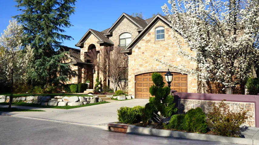 Stone exterior with arched entryways, wood-finish garage door, mature landscaping, and an integrated stone retaining wall