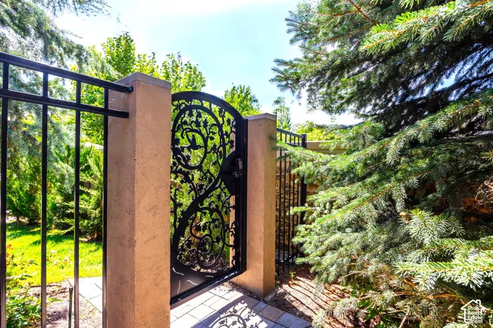 Wrought iron gate with ornate detailing, flanked by stucco-finished pillars and a matching wrought iron fence