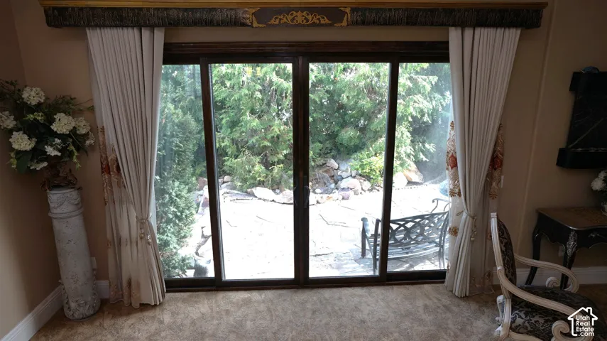 Sliding glass door opening to a paved patio, surrounded by mature greenery