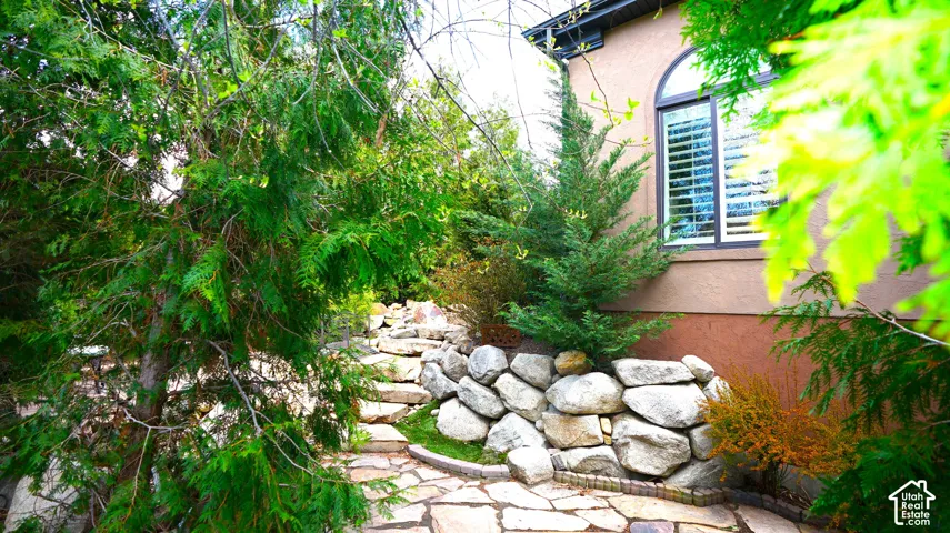 Stone pathway with natural stone steps and retaining wall, complemented by mature evergreen landscaping and a stucco exterior with an arched window
