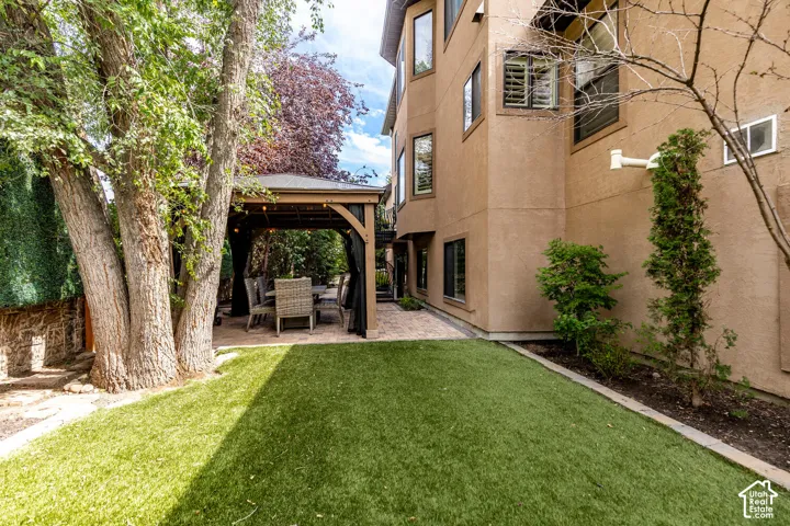 Backyard featuring artificial turf, a paved patio, and a built-in gazebo with string lighting