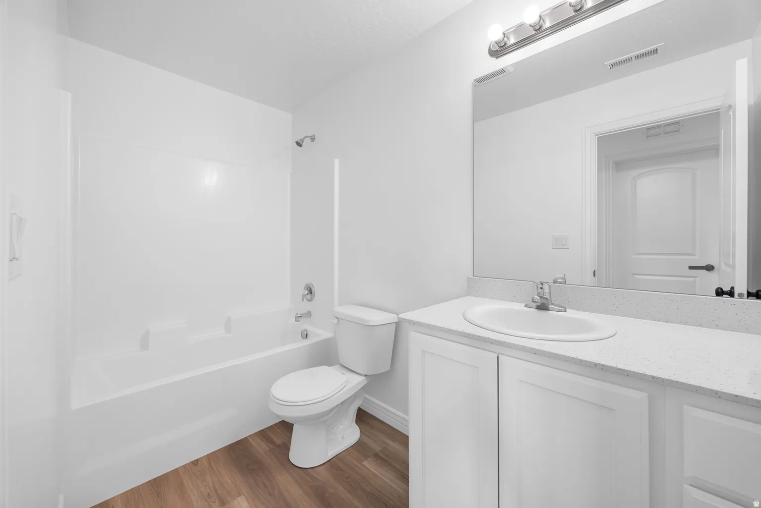 Bathroom featuring a white vanity with an undermount sink, a large mirror, a chrome light fixture, a white toilet, and wood-finish flooring
