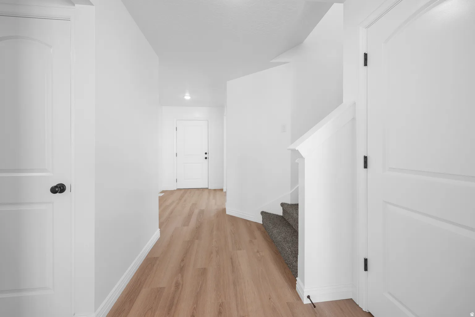 Wood-finish flooring, white paneled doors, matte black door hardware, white walls, and a carpeted staircase