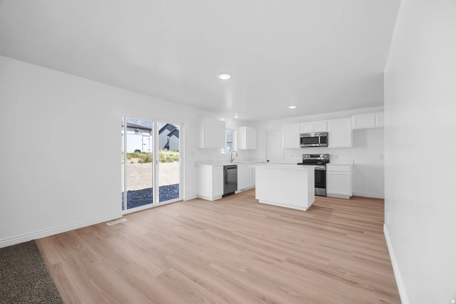 Open-concept living area featuring wood-finish flooring, white cabinetry, a kitchen island, stainless steel appliances, and sliding glass doors