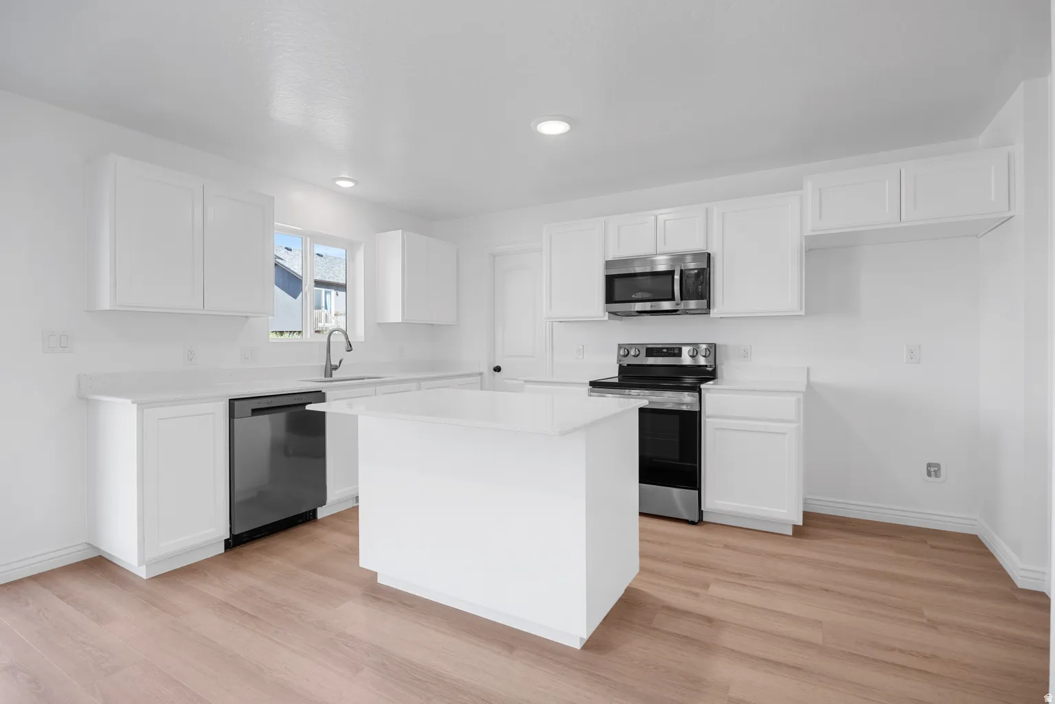 Contemporary kitchen featuring white cabinetry, light-toned wood-finish flooring, a central island, and stainless steel appliances