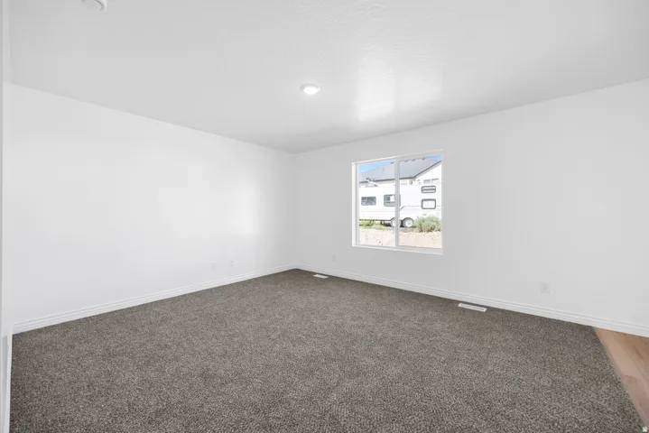 Recessed ceiling light, white painted walls, gray carpeting, wood-finish flooring, and a single window with white trim