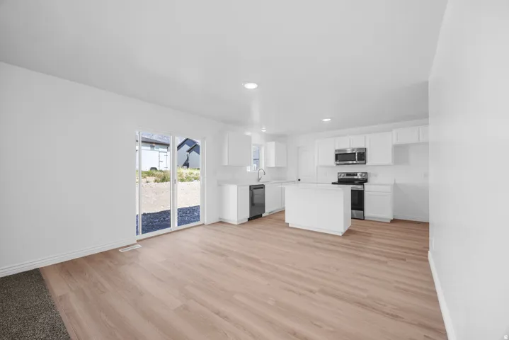 Open-concept living area featuring wood-finish flooring, white cabinetry, a kitchen island, stainless steel appliances, and sliding glass doors