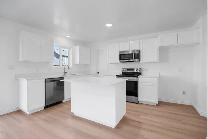 Contemporary kitchen featuring white cabinetry, light-toned wood-finish flooring, a central island, and stainless steel appliances