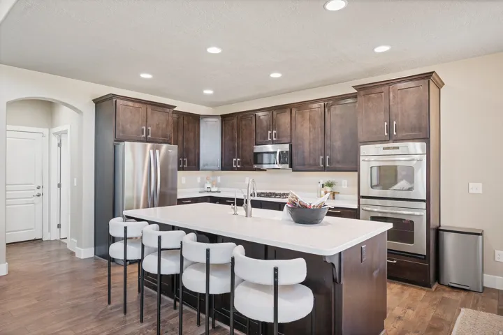 Expansive kitchen featuring wood-finish flooring, dark wood cabinetry, stainless steel appliances, a center island with a light-toned countertop, and recessed lighting