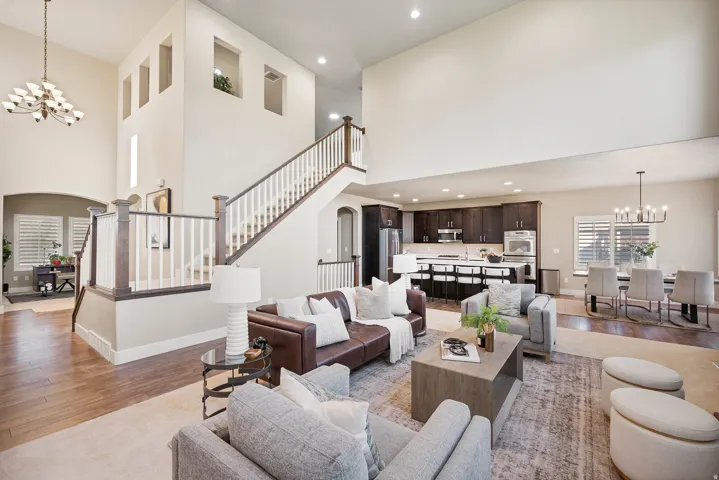 Two-story living area with high ceilings, wood-finish flooring, and a grand staircase featuring white spindles and dark wood handrails