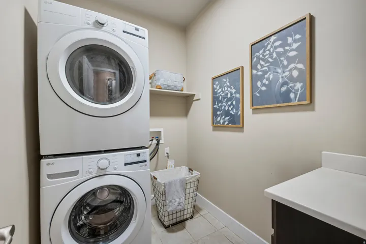 Stacked washer and dryer, built-in shelving, tile flooring, and a countertop with dark cabinetry