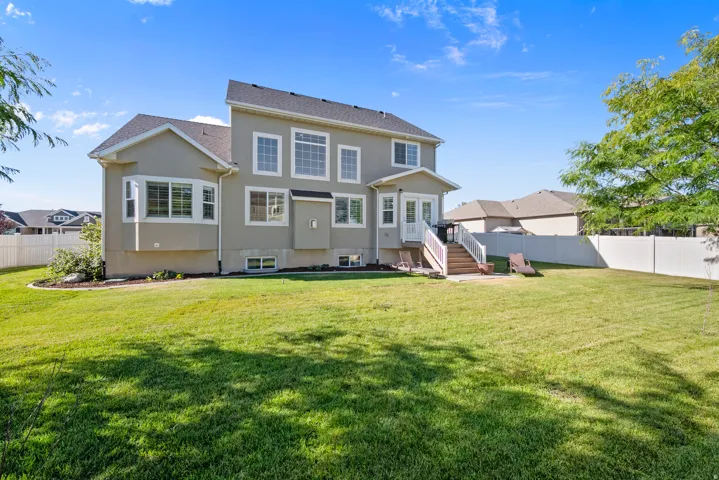 Expansive rear yard with a manicured lawn, full privacy fencing, and mature trees