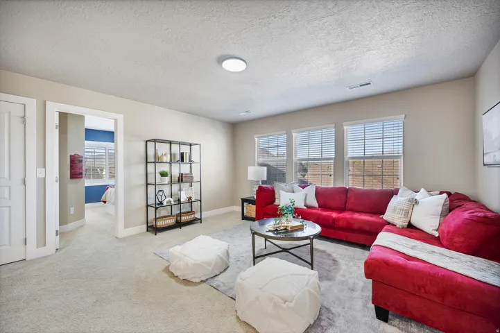 Recessed ceiling lighting, three windows with horizontal blinds, light-colored carpeting, and an open doorway