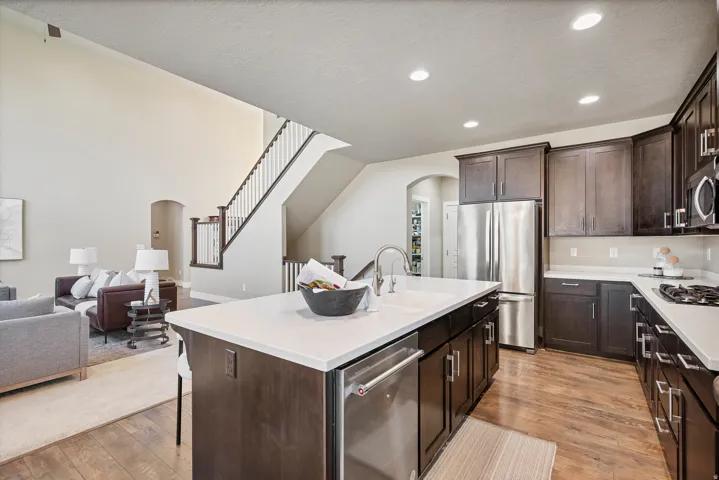Kitchen with an expansive island featuring an integrated sink, dark wood-finish cabinetry, stainless steel appliances, and light-toned countertops