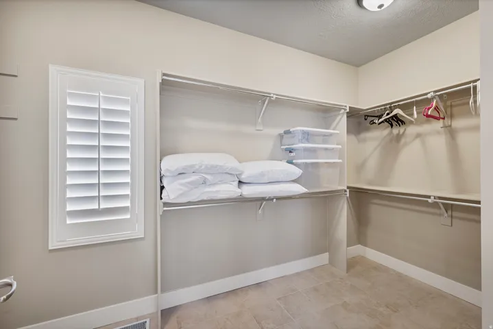 Expansive closet with organized shelving and hanging rods, featuring a window with white plantation shutters and neutral wall paint