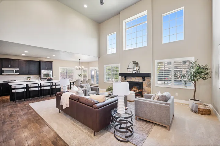 Open-concept living space with vaulted ceilings, large windows, a stone-clad fireplace, and wood-finish flooring