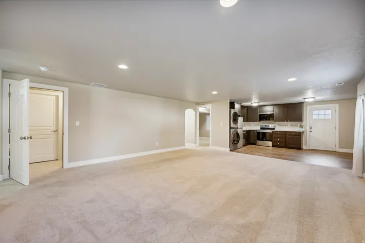 Expansive open-concept living space with recessed lighting, carpet flooring, and a full kitchen featuring wood-finish cabinetry, white countertops, and stainless steel appliances