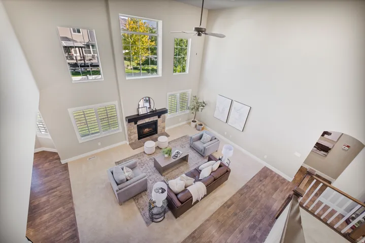 Two-story living room with a ceiling fan, stone-faced fireplace with a wood mantel, and large windows