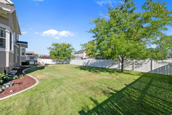 Expansive backyard featuring a manicured lawn, a mature shade tree, a white privacy fence, and a multi-level deck with white railings