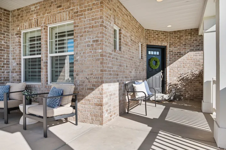 Covered porch featuring brick exterior, white window frames, and a dark entry door with transom lites
