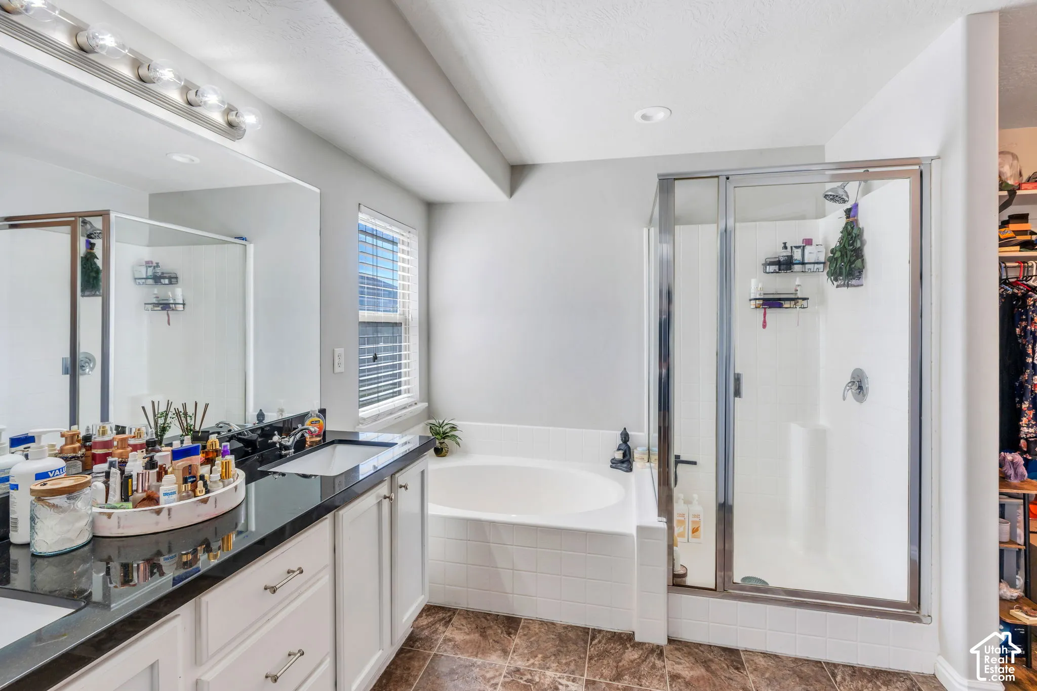 Primary Bathroom with Dual sink vanity with dark-tone countertop, built-in bathtub, and glass-enclosed shower.