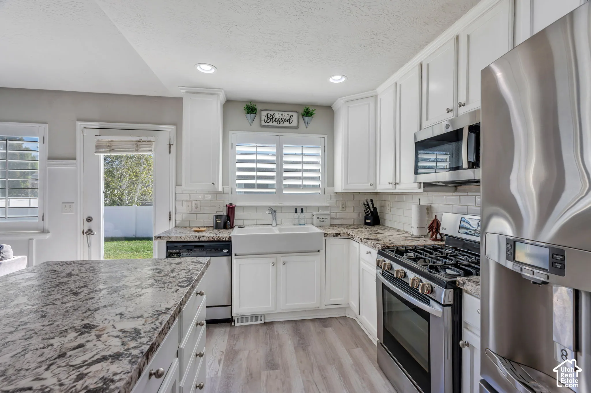 White cabinetry with crown molding, stainless steel appliances, wood-finish laminate flooring, white subway tile backsplash, and a farmhouse sink