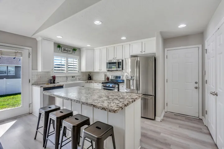 White shaker cabinetry, stainless steel appliances, white subway tile backsplash, light-toned wood-finish laminate flooring, and a large central island