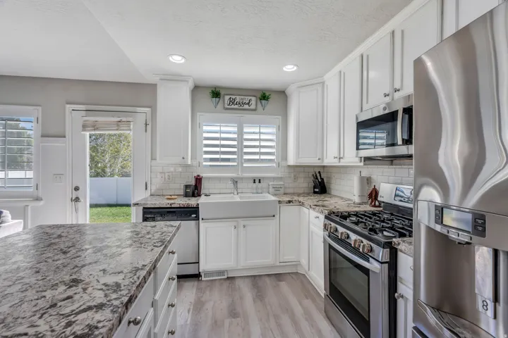 White cabinetry with crown molding, stainless steel appliances, wood-finish laminate flooring, white subway tile backsplash, and a farmhouse sink