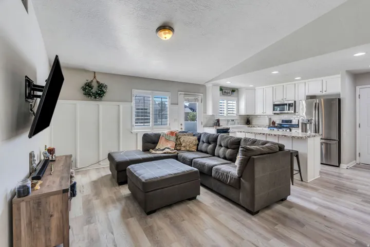 Open-concept living area with wood-finish flooring, board and batten wall detailing, and a kitchen featuring white cabinetry, a tile backsplash, and stainless steel appliances