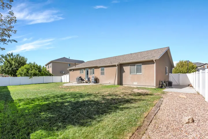 Expansive backyard featuring a manicured lawn, white privacy fencing, a concrete patio, and a gravel pathway with concreted area that could be used as a dog run.