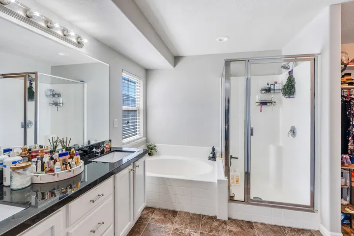 Primary Bathroom with Dual sink vanity with dark-tone countertop, built-in bathtub, and glass-enclosed shower.