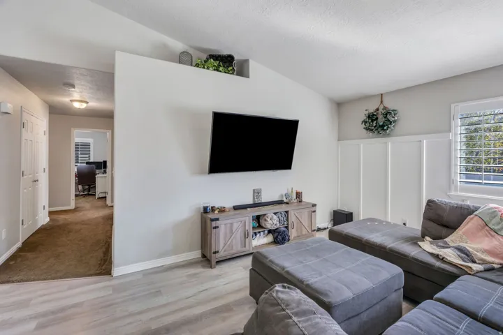 Light wood-finish laminate flooring, accent wall with wainscoting, white window shutters, and a sloped ceiling