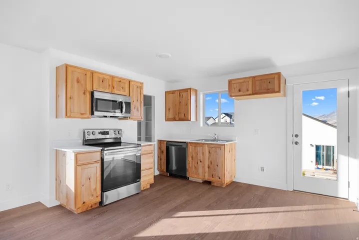Wood-finish flooring, light wood cabinetry, stainless steel appliances, white countertops, and a glass-paneled exterior door