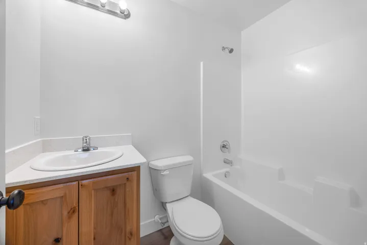 White bathtub with integrated shower, wood-finish vanity with an integrated sink, and a chrome faucet