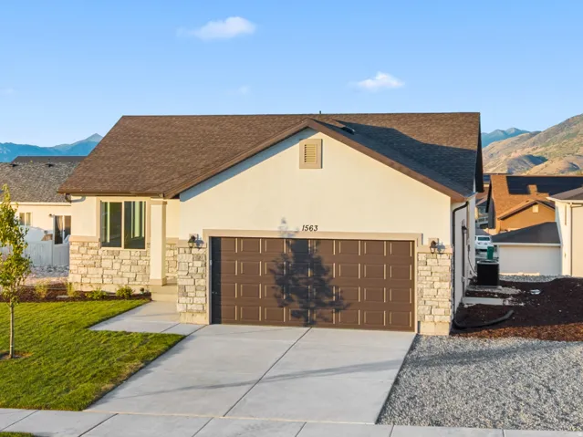 Contemporary stucco exterior with stone accents, a two-car garage, concrete driveway, and established front landscaping