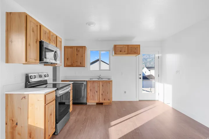 Kitchen featuring wood-finish cabinetry, stainless steel appliances, white countertops, and wood-finish flooring