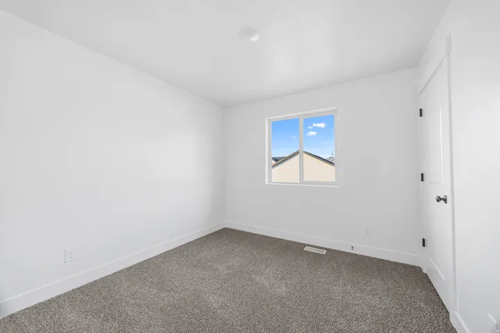 Neutral wall finishes complemented by plush carpeting, a single window, and a paneled door with dark hardware