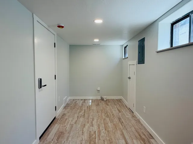 Recessed lighting illuminates the wood-finish flooring in this versatile space, featuring multiple windows and a contemporary door handle