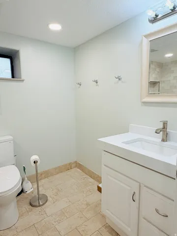 Recessed ceiling lighting, vanity with an integrated sink, wall-mounted mirror with overhead lighting, and tiled flooring
