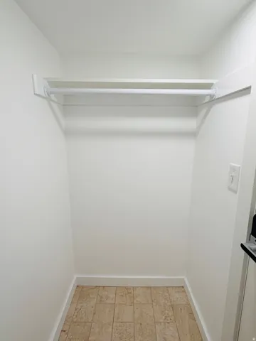 Built-in closet shelving with hanging rod, light-toned tile flooring, and crisp white walls
