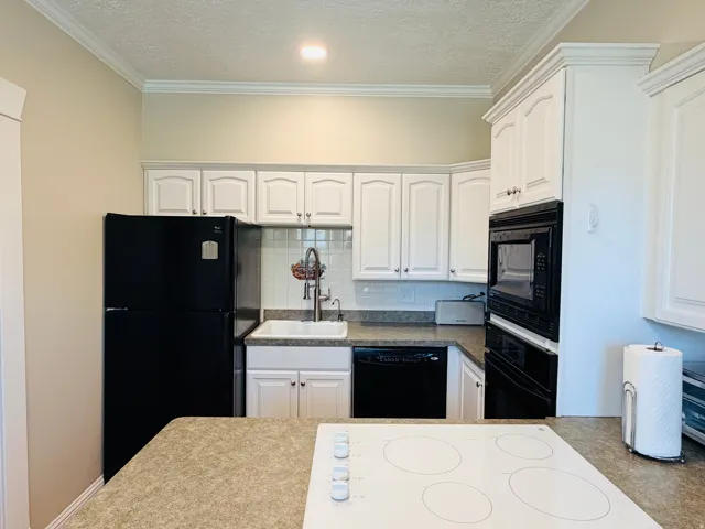 White cabinetry with crown molding, integrated wall oven and microwave, dark countertops, white tile backsplash, and a built-in cooktop