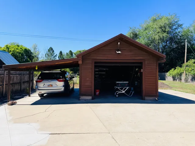 Detached garage with a single bay door, wood siding, and a covered carport extension