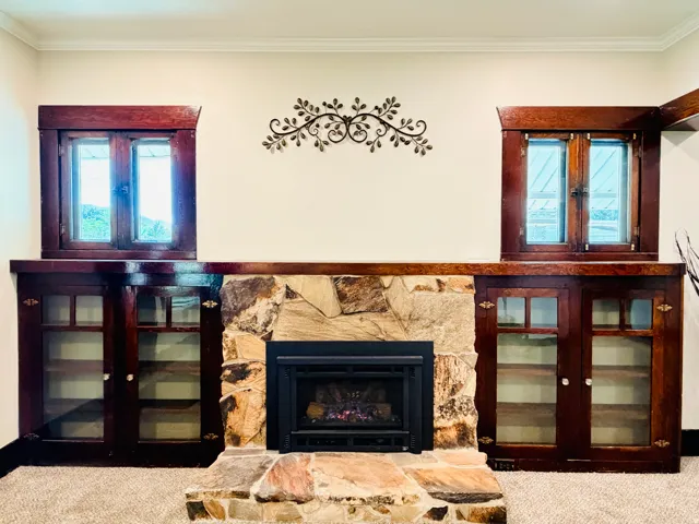 Stone-clad fireplace with a built-in electric insert, flanked by custom wood cabinetry with glass-front doors, and wood-framed windows