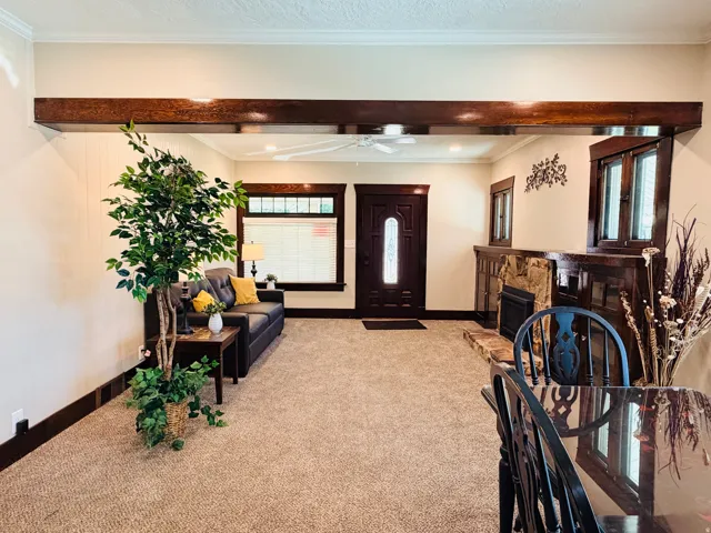 Exposed wood beam, stone-surround fireplace, dark wood trim, ceiling fan, and decorative front entry door