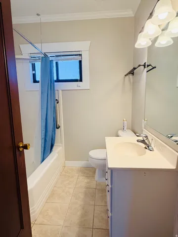 Bathroom featuring a white vanity with integrated sink, tiled flooring, a bathtub with a shower, and a mirror with overhead lighting