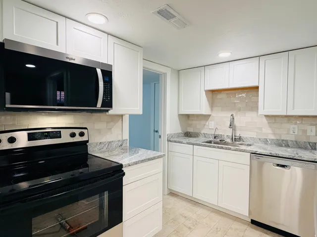 Kitchen featuring white shaker-style cabinetry, light-toned tile flooring, light-colored subway tile backsplash, and stainless steel appliances including a microwave and dishwasher