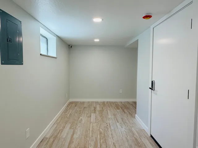 Recessed lighting, wood-finish flooring, light grey painted walls, and a white interior door